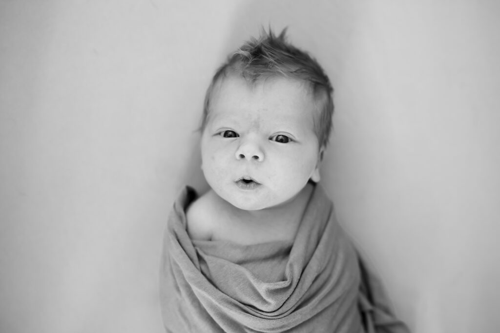 Wakeful baby boy in swaddle looking up at photographer