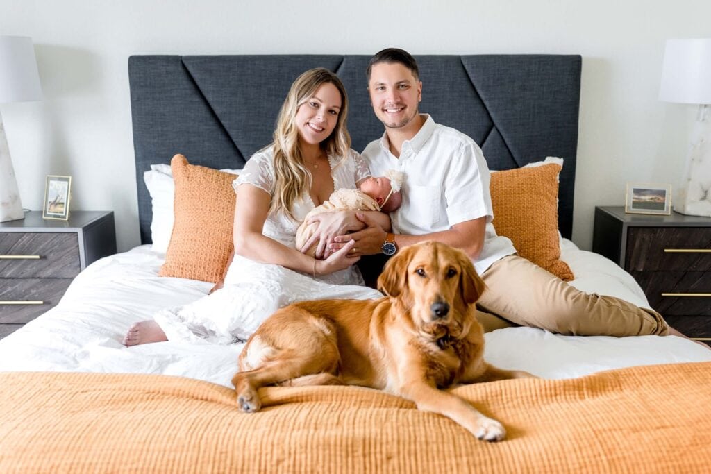 Parents holding newborn on bed at home in Peyton Colorado with family dog next to them