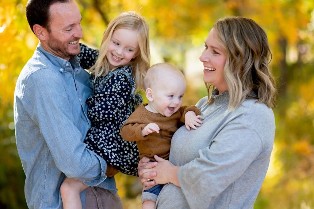 Parents holding children and smiling with fall foliage in the background