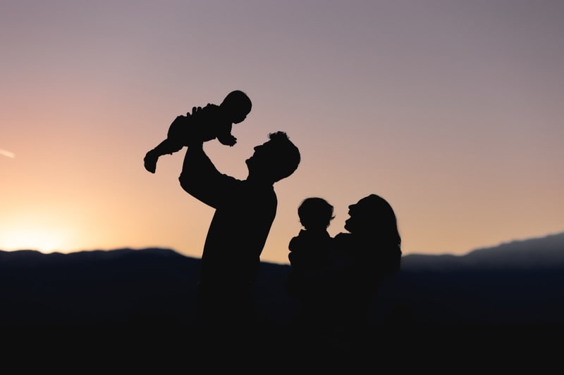 Sunset silhouette of family with dad holding baby in the air