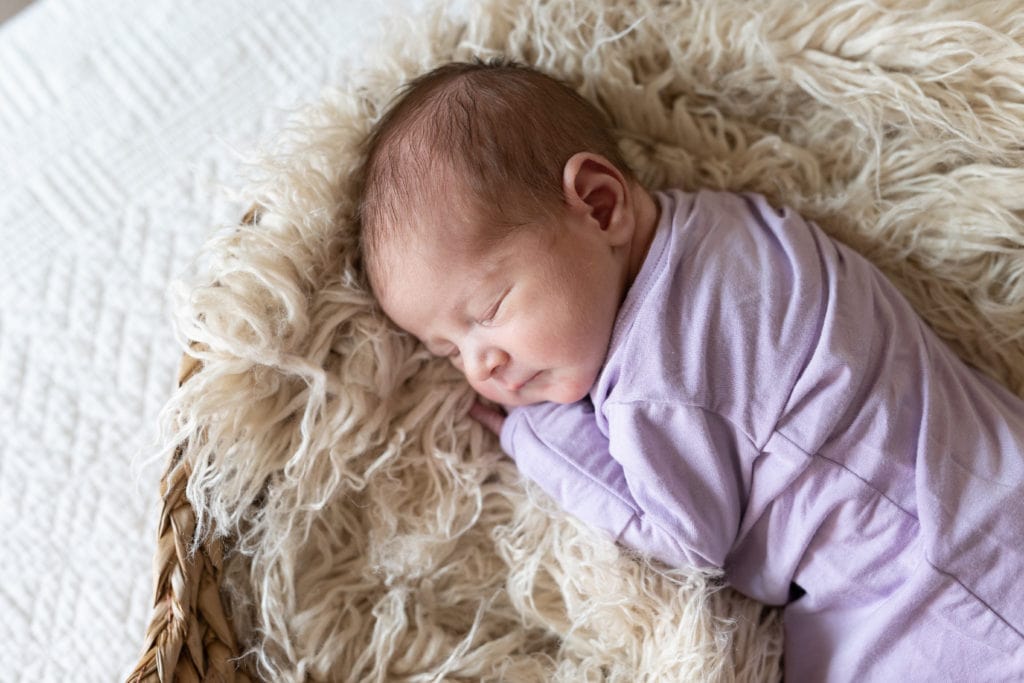 Up close image of sleeping baby lying on a faux fur blanket, cuddled over onto her side as part of a newborn photoshoot