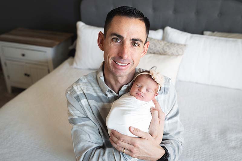 Father holding his newborn daughter on bed with white and gray backdrop