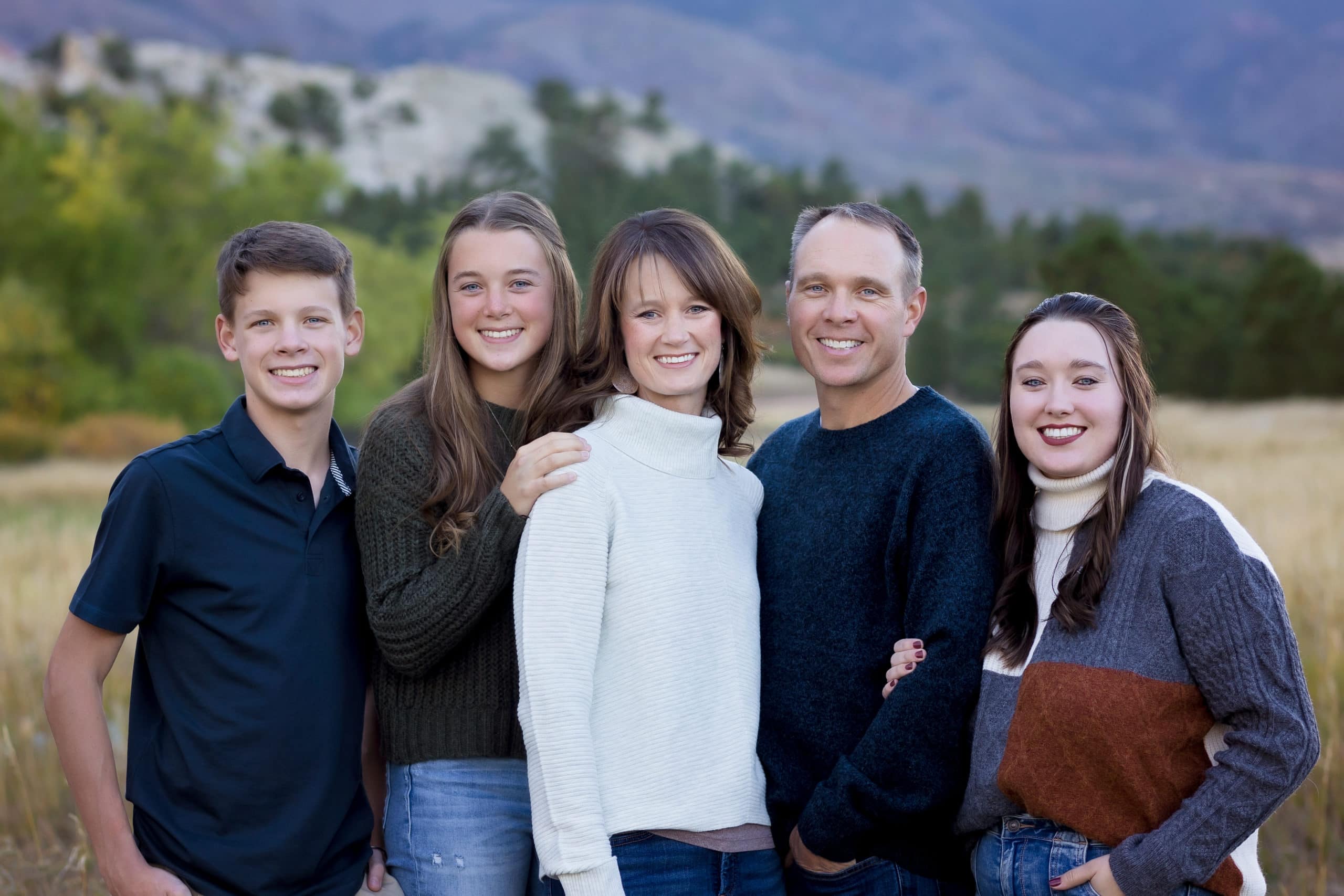 large family with teen children huddles together for winter family portraits in front of colorado mountain views