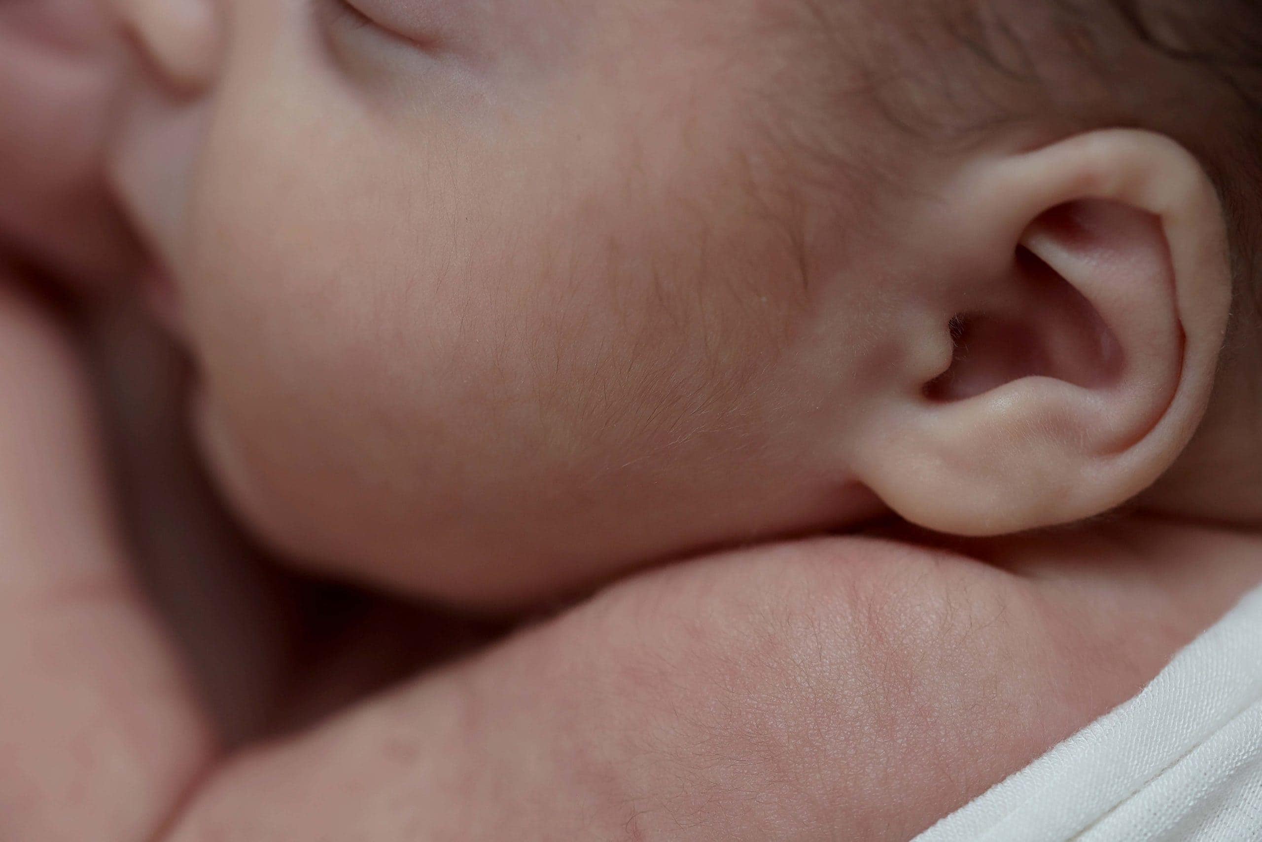 up close image of details of a newborn's skin and facial features taken from the side perspective, showing their eyelashes, nose, and ears