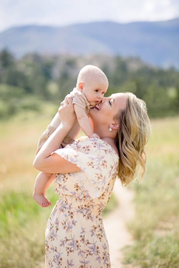 Laughing young woman holds her baby up for a kiss in a beautiful landscape in Colorado