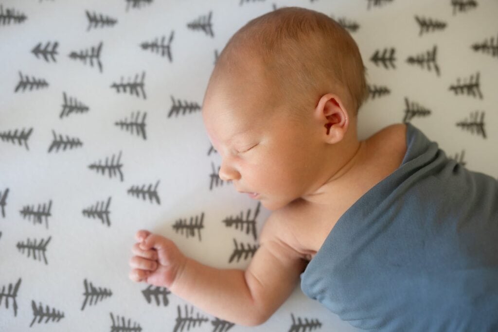 Infant in blue swaddle asleep in crib in home nursery