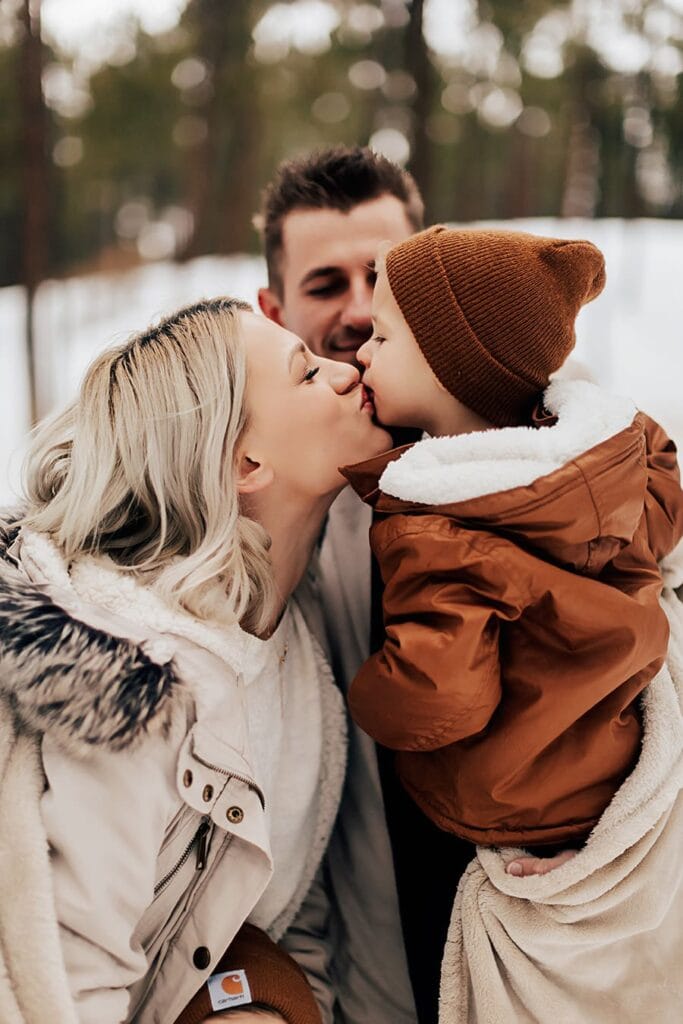 Mom kissing young son against winter backdrop