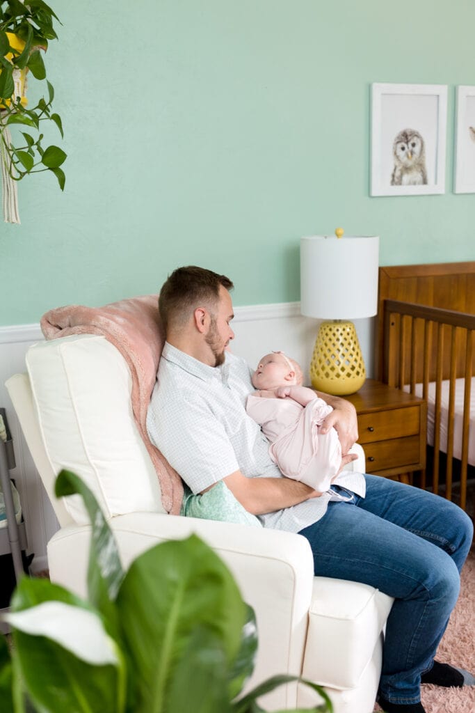 Father sitting in armchair in nursery holding infant daughter