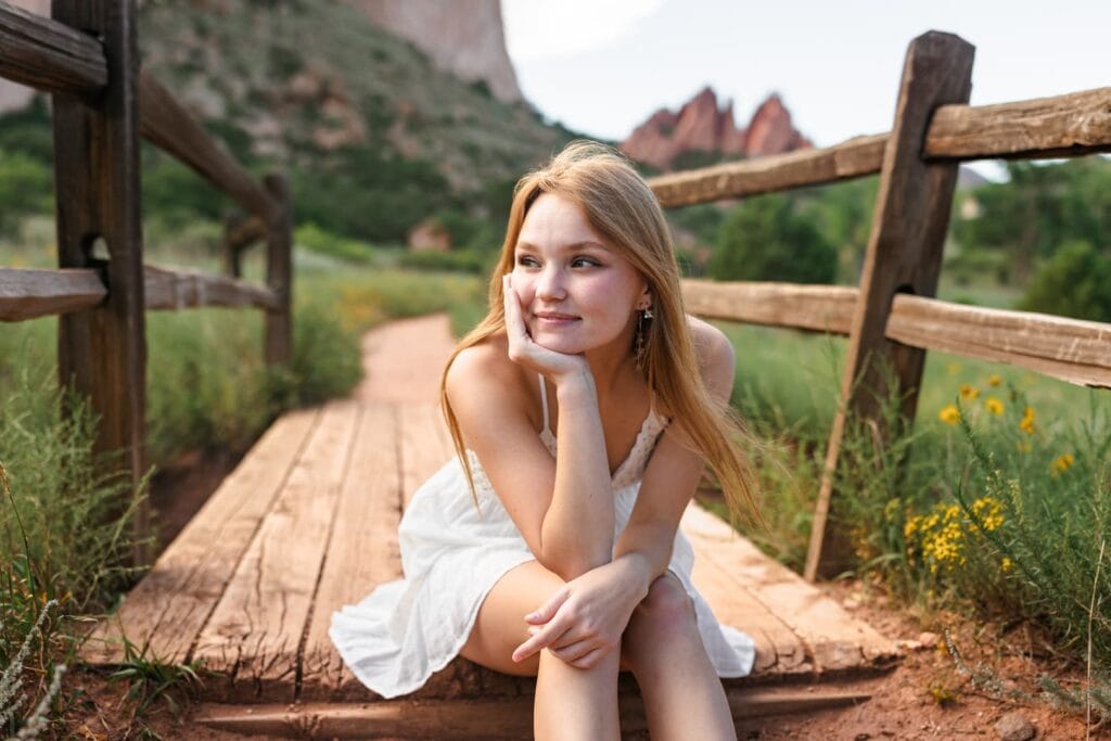 Teen girl in sundress sitting on bridge with hills in backdrop and gazing into the distance