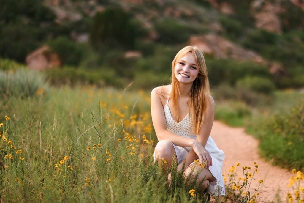 High school senior girl in white sundress kneeling among yellow flowers in Garden of the Gods, Colorado Springs