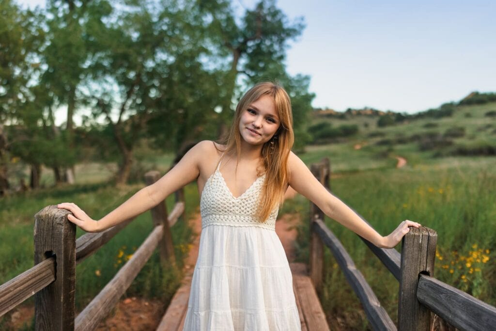 High school senior girl standing on bridge in meadow