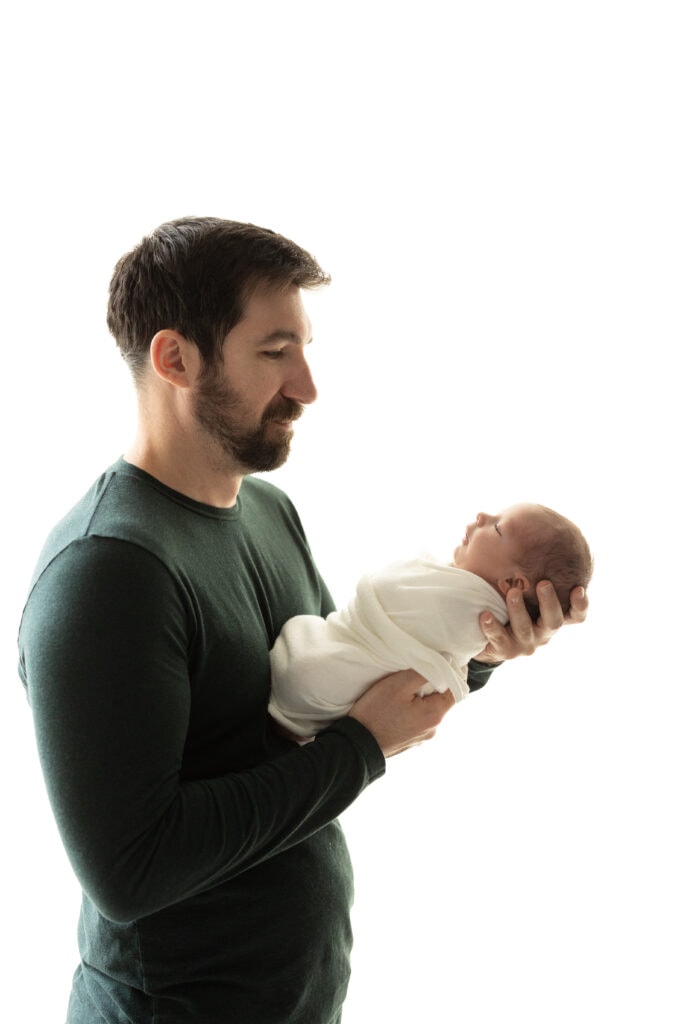 Father holding baby boy securely against natural light backdrop in Colorado Springs photo studio