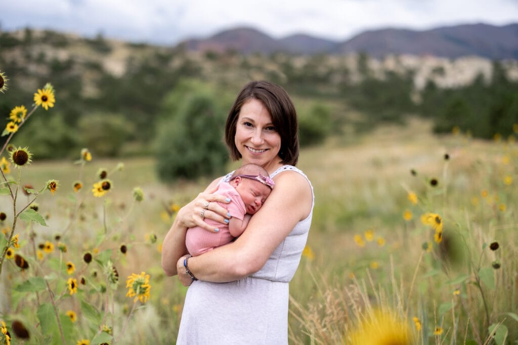 Mother standing in a field of sunflowers near Colorado Springs, holding newborn baby girl