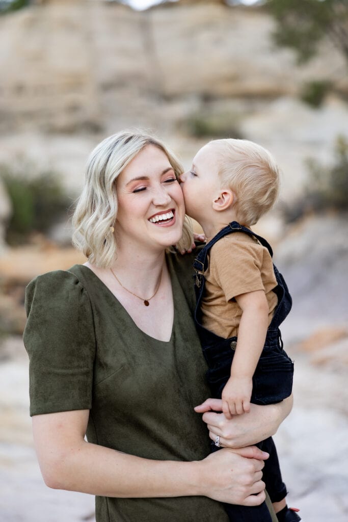 Mom laughing while toddler son kisses her cheek