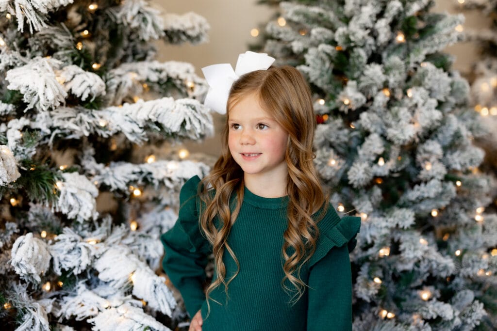 Little girl in green dress standing among Christmas trees in Colorado Springs studio
