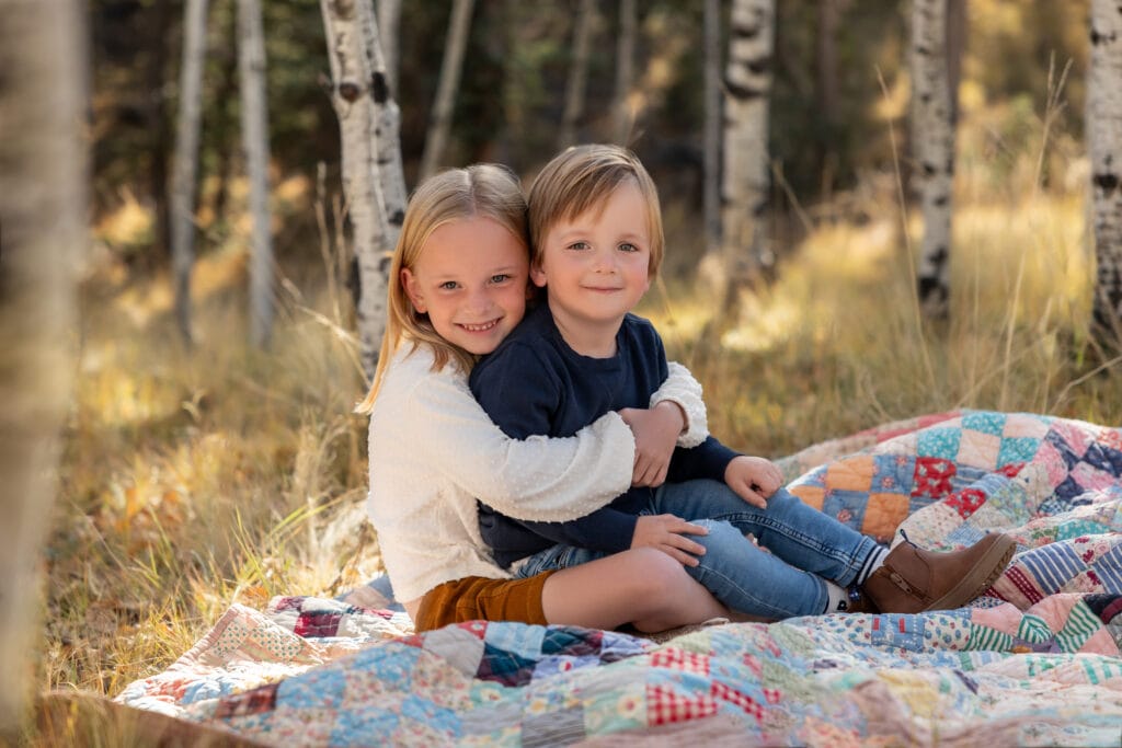 Young siblings seated on patchwork quilt in a grove of aspen trees in Woodland Park Colorado