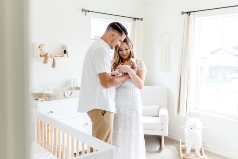 Parents cuddle close together with their newborn in nursery decorated with neutral colors