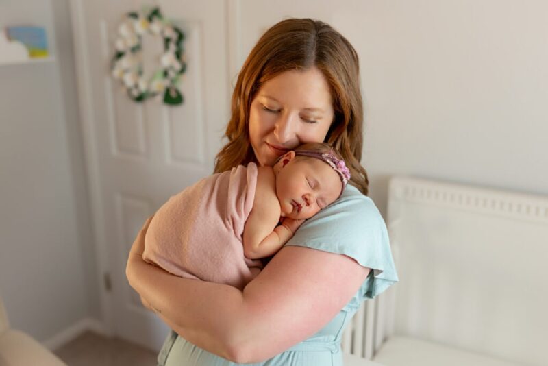 tips for newborn photography safety, mom cradling baby girl in nursery