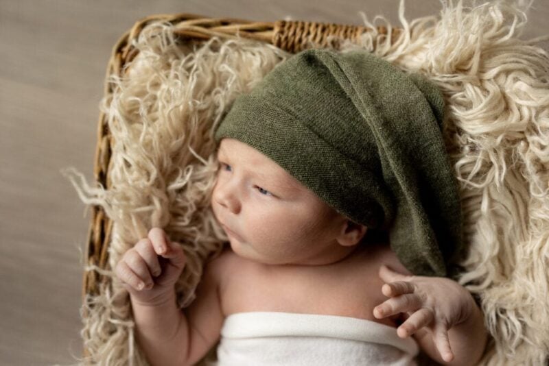 Baby in olive green hat lying in basket