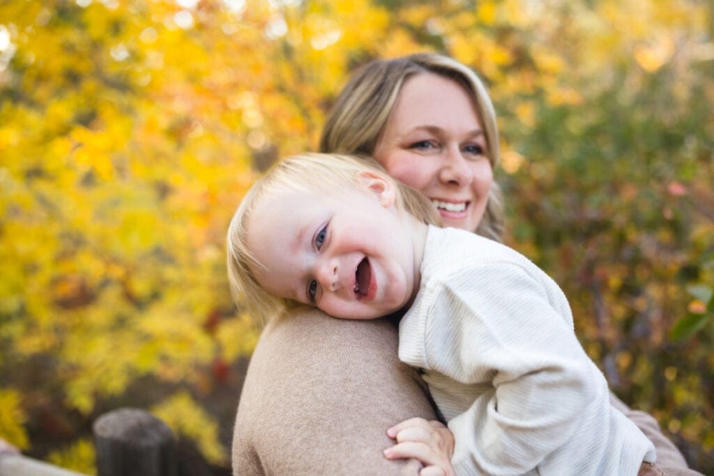 mom hugging child against fall foliage backdrop