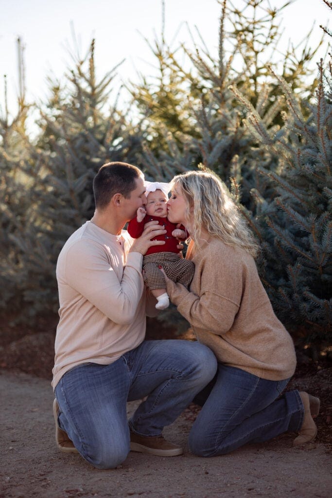 Parents kissing baby girl at Colorado Springs Christmas tree farm