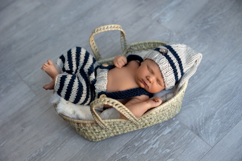 Baby boy in striped gray and black outfit asleep in basket on the floor