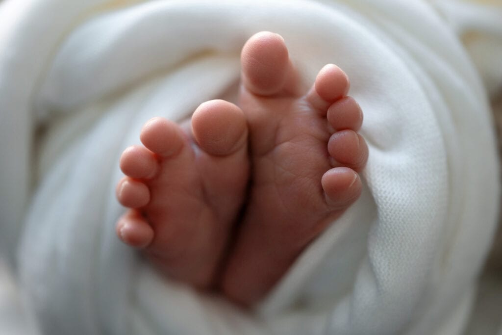 Closeup of newborn baby's toes poking out of white swaddle