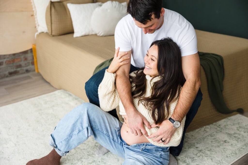Man seated on bed with pregnant woman leaning against his legs