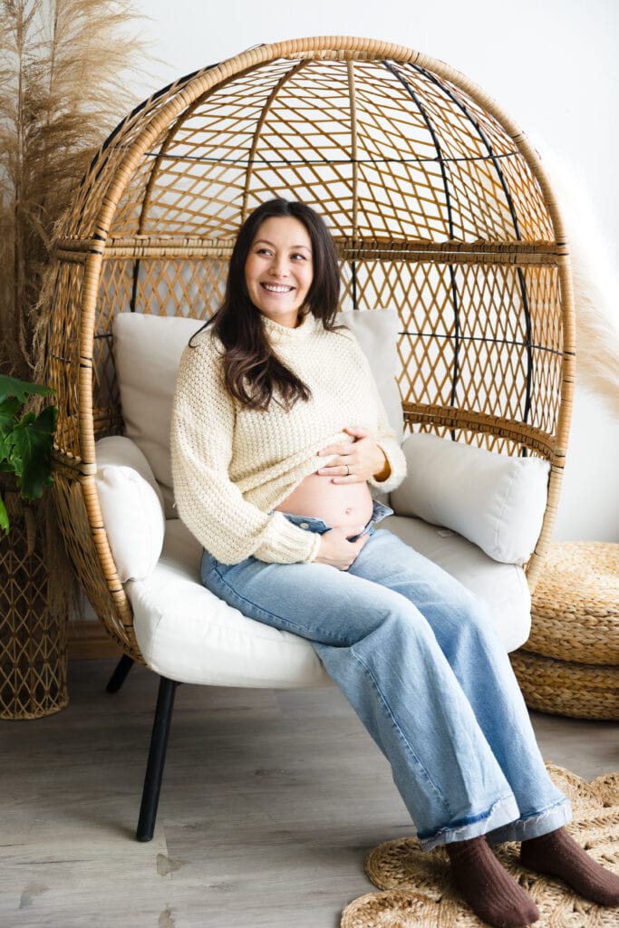 Pregnant woman seated in wicker egg chair with her hands on her belly