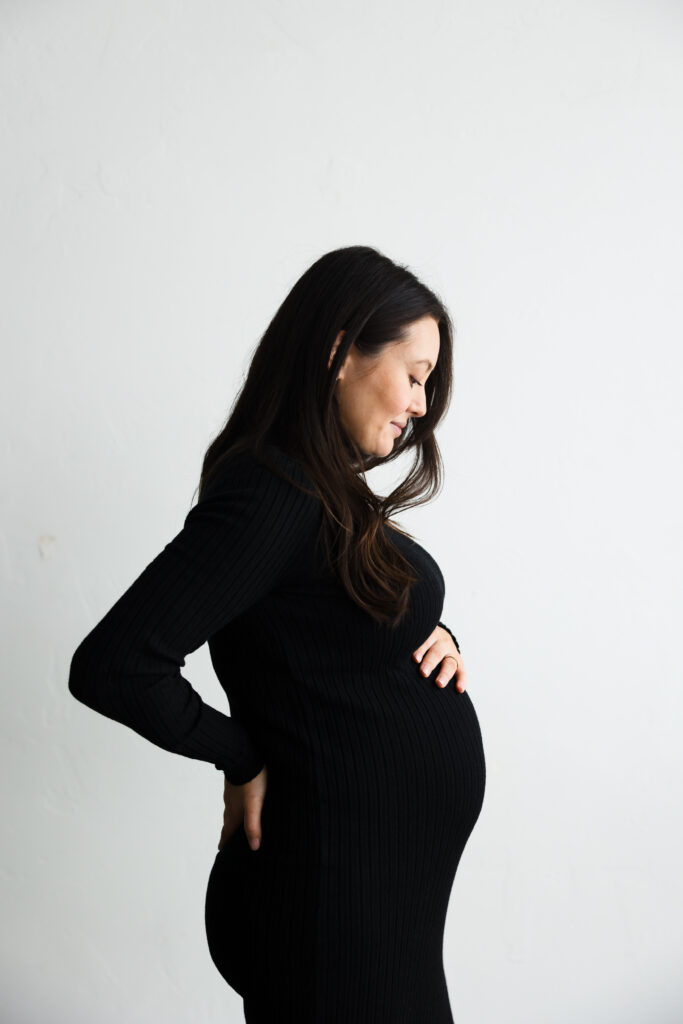 Woman in black maternity gown against white backdrop