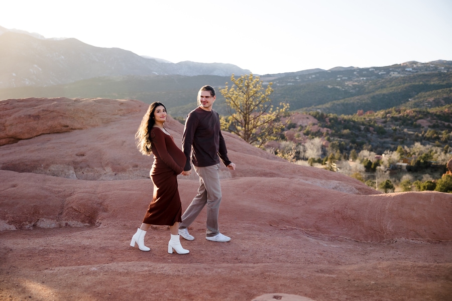 Couple walking across red rocks with mountain backdrop in Garden of the Gods